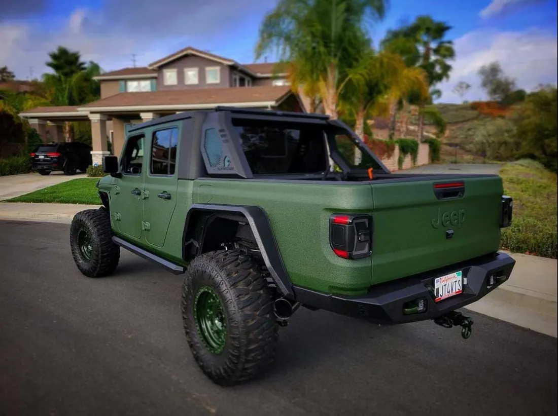 A Jeep Gladiator coated in a flat military green textured coating over the entire body, with black wheels and a steel rear bumper.