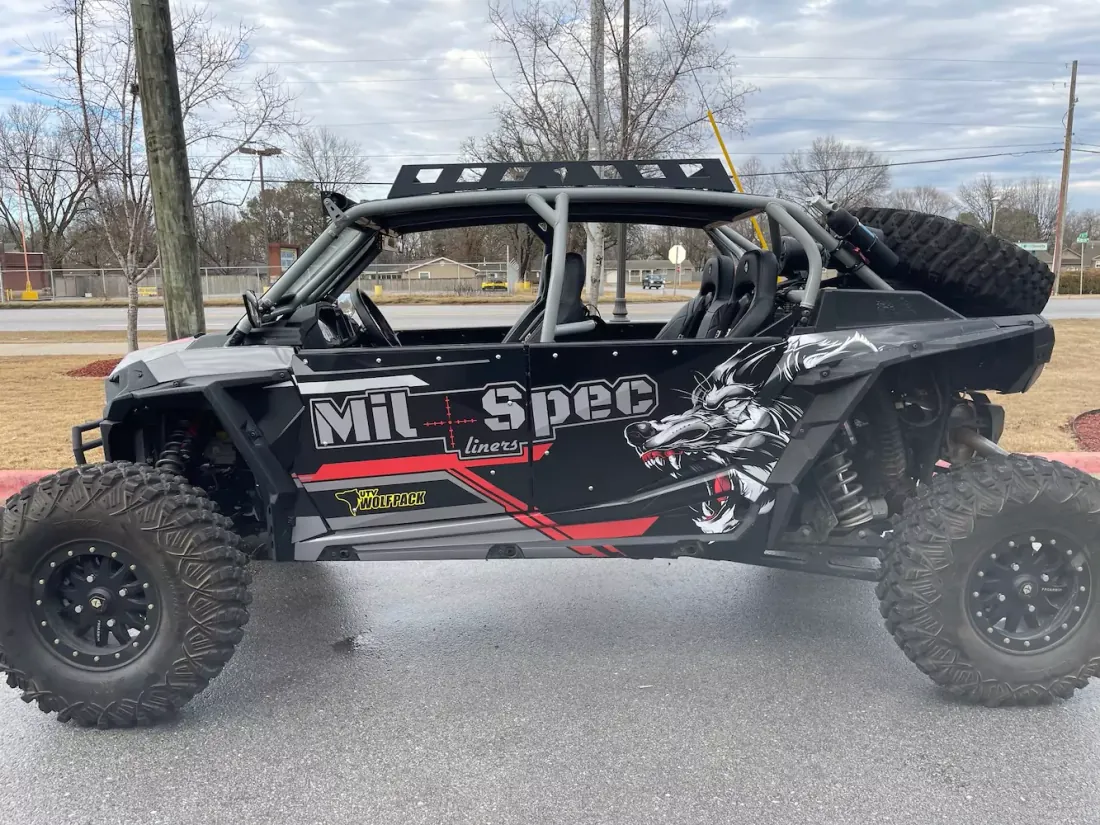 A Polaris side by side UTV with a two tone coated body, roll cage and spare tire mounted at the rear.