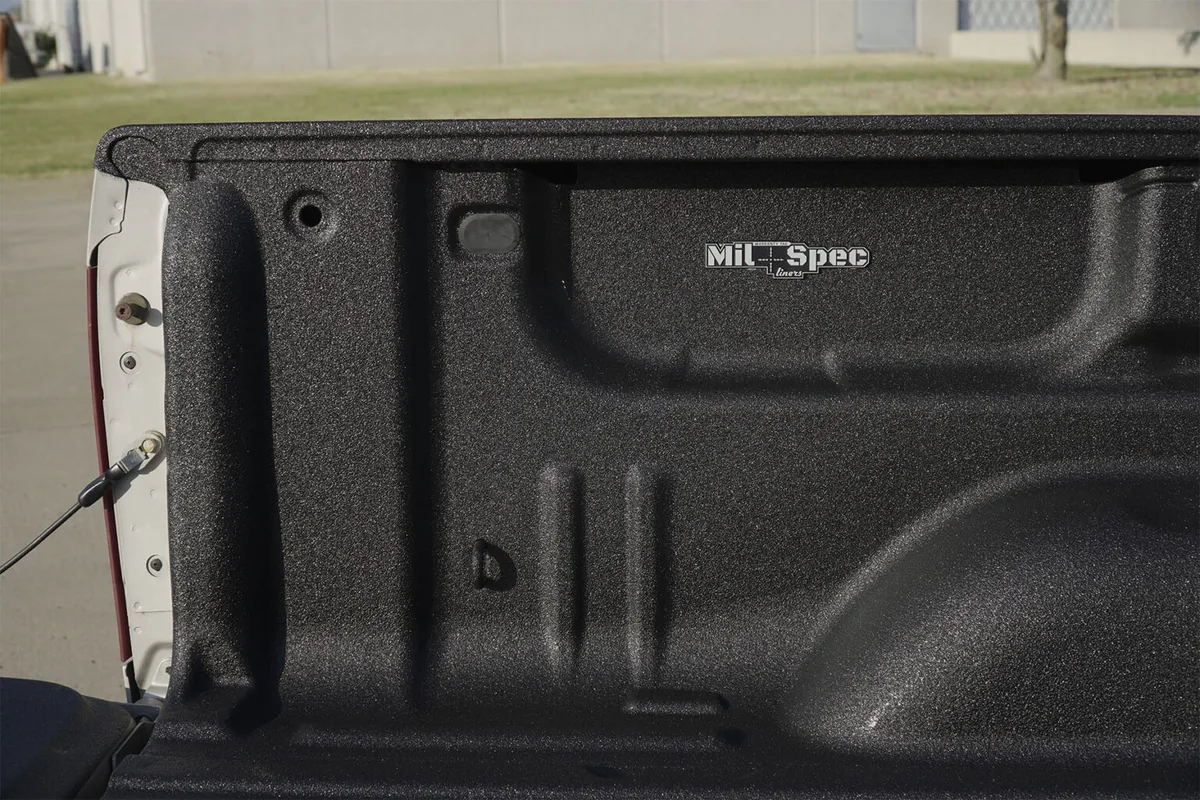 Close-up of a sprayed black textured bed liner on a truck bulkhead, with the Mil-Spec Liner mark visible in the coating.